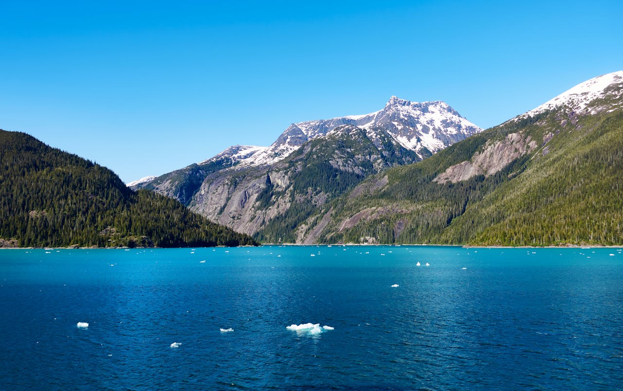 Services Stunning view of a turquoise lake surrounded by snow-capped mountains in Alaska under a clear blue sky.